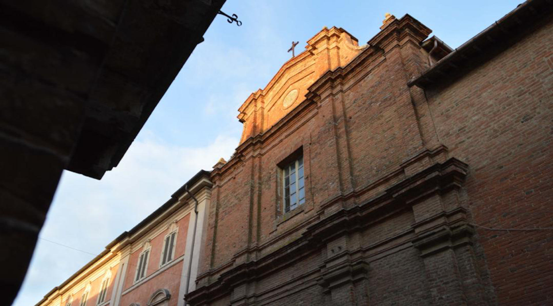 Façade of a brick church at sunset, with well-preserved architectural details, viewed from below.