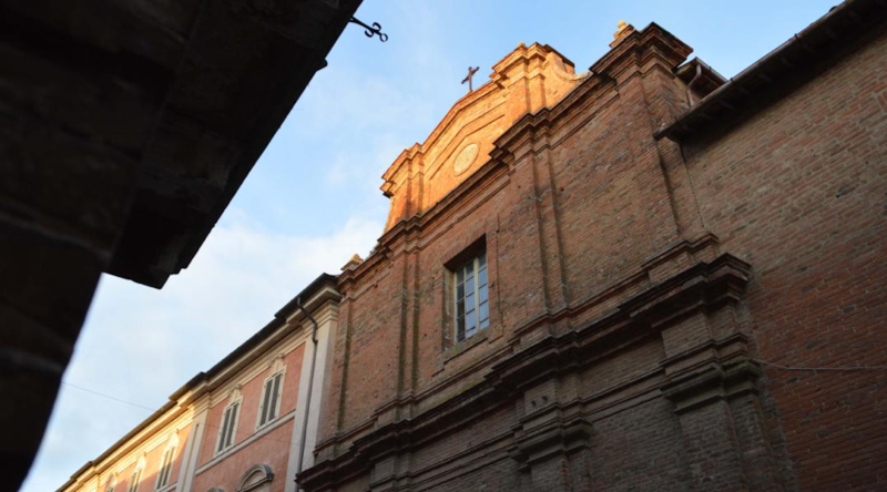 Facciata di una chiesa in mattoni al tramonto, con dettagli architettonici ben conservati, vista dal basso.