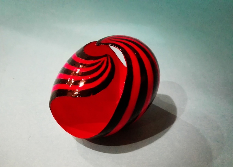 Œuf décoré de peinture rouge et noire, sculpté avec un motif en spirale qui crée un effet dynamique et moderne.
