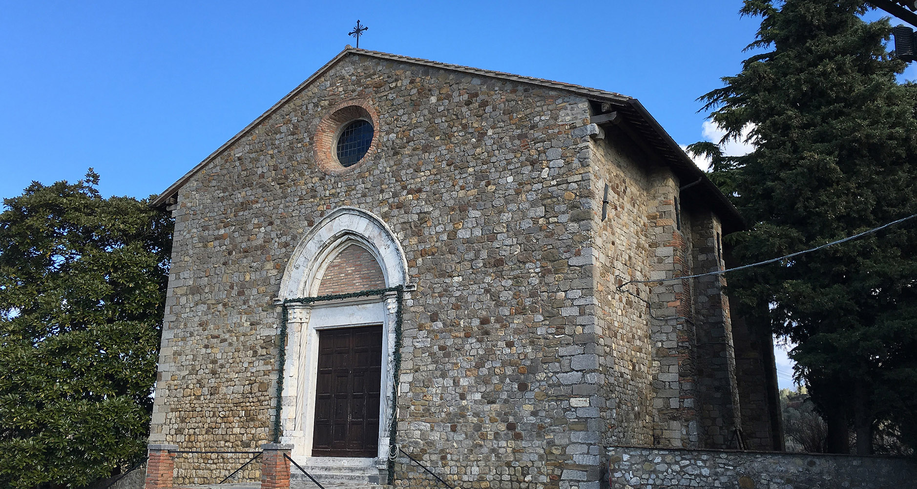 Stone façade of the Church of Santa Maria Vecchia in Ficulle, with a Gothic portal and a small circular rose window.