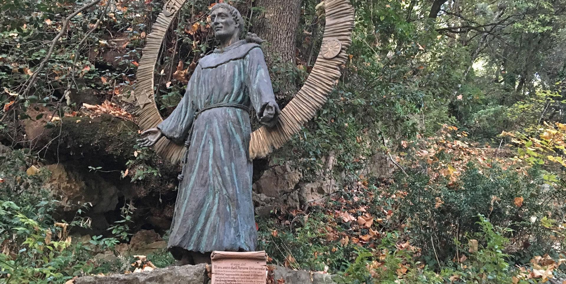 Statue of Saint Francis, surrounded by greenery, with open arms as a sign of welcome and spirituality.