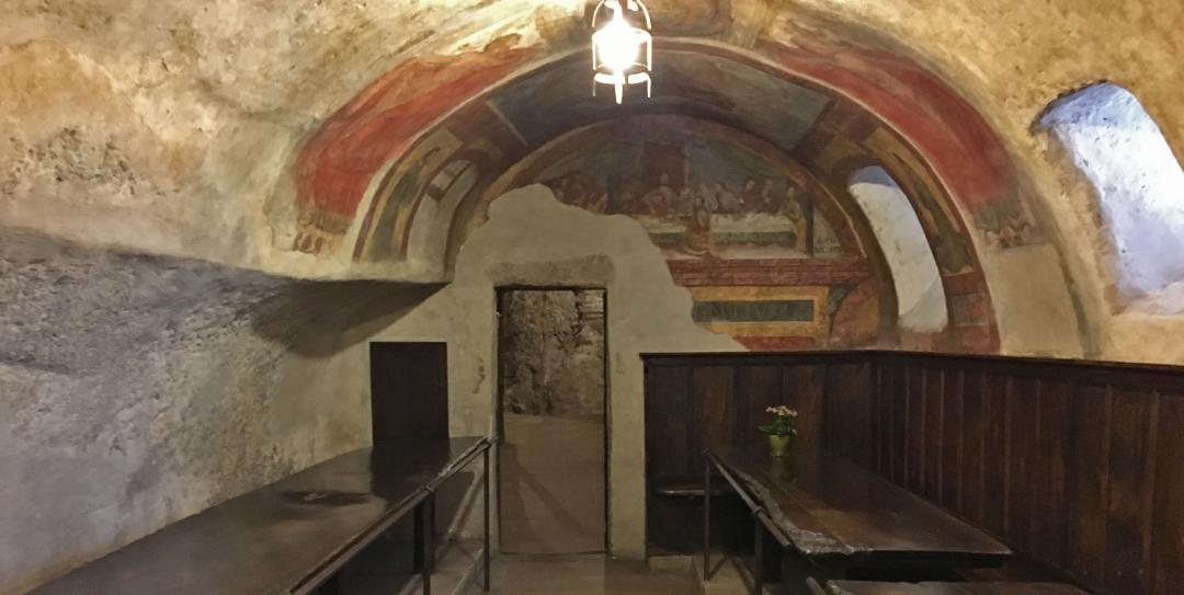 Speisesaal des Eremo delle Carceri, in den Felsen gehauen, mit alten Fresken und schlichten Holzmöbeln.