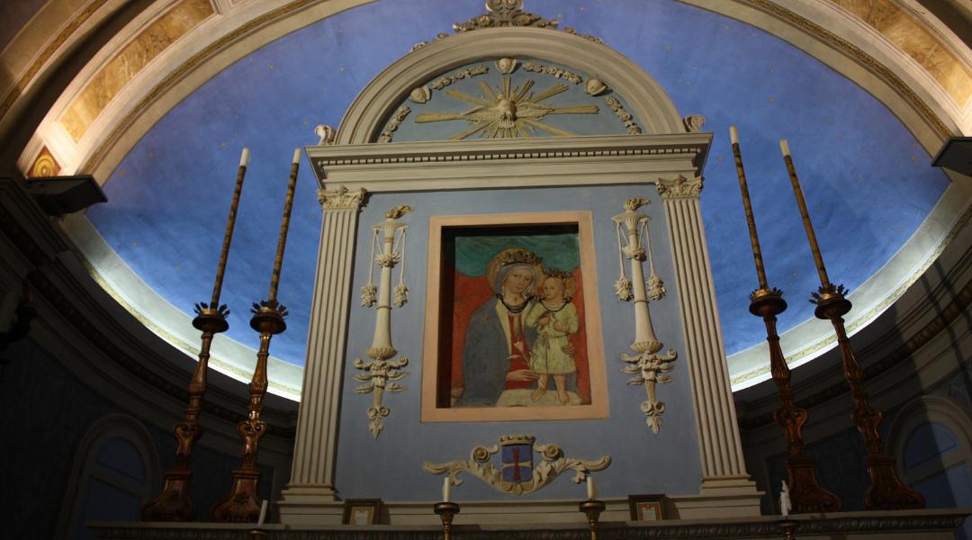 Altar mit einem Bild der Madonna mit Kind, eingerahmt von Säulen und Kerzenhaltern, unter einem halbrunden blauen Gewölbe.