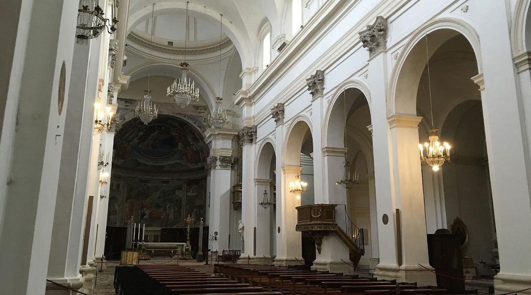 Interno del Duomo di Spoleto con navata bianca, lampadari a candelabro, pulpito ligneo e affreschi sull'abside.