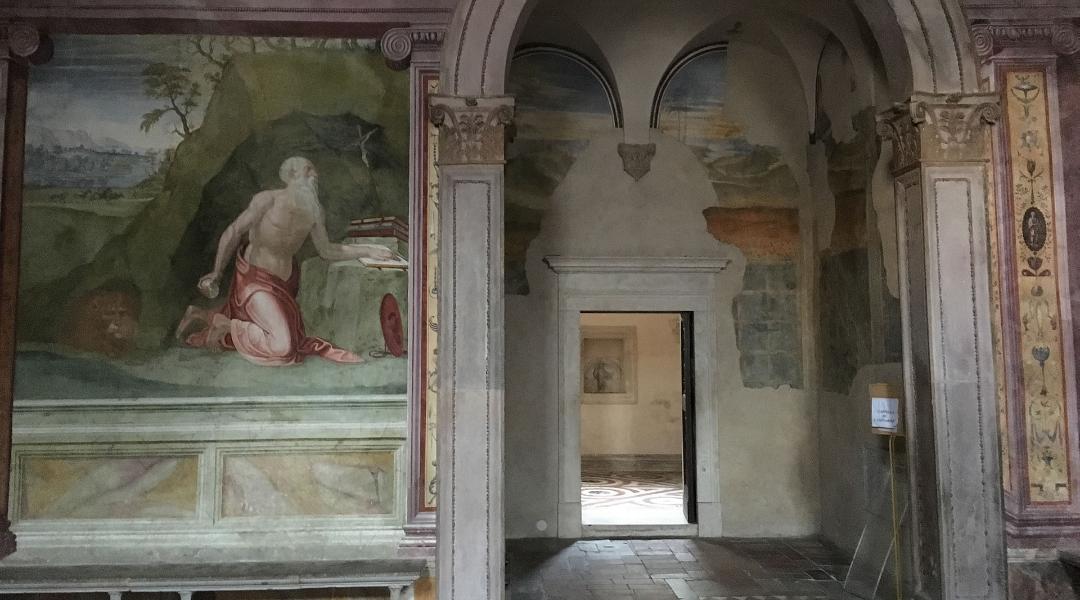 Affresco rinascimentale nella Cattedrale di Spoleto con San Girolamo in preghiera, colonne decorate e porta aperta su un'altra sala.