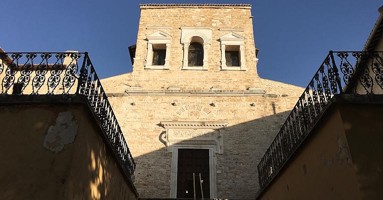 Stone façade of the Basilica of San Salvatore with steps and iron balustrades, lit by the setting sun.
