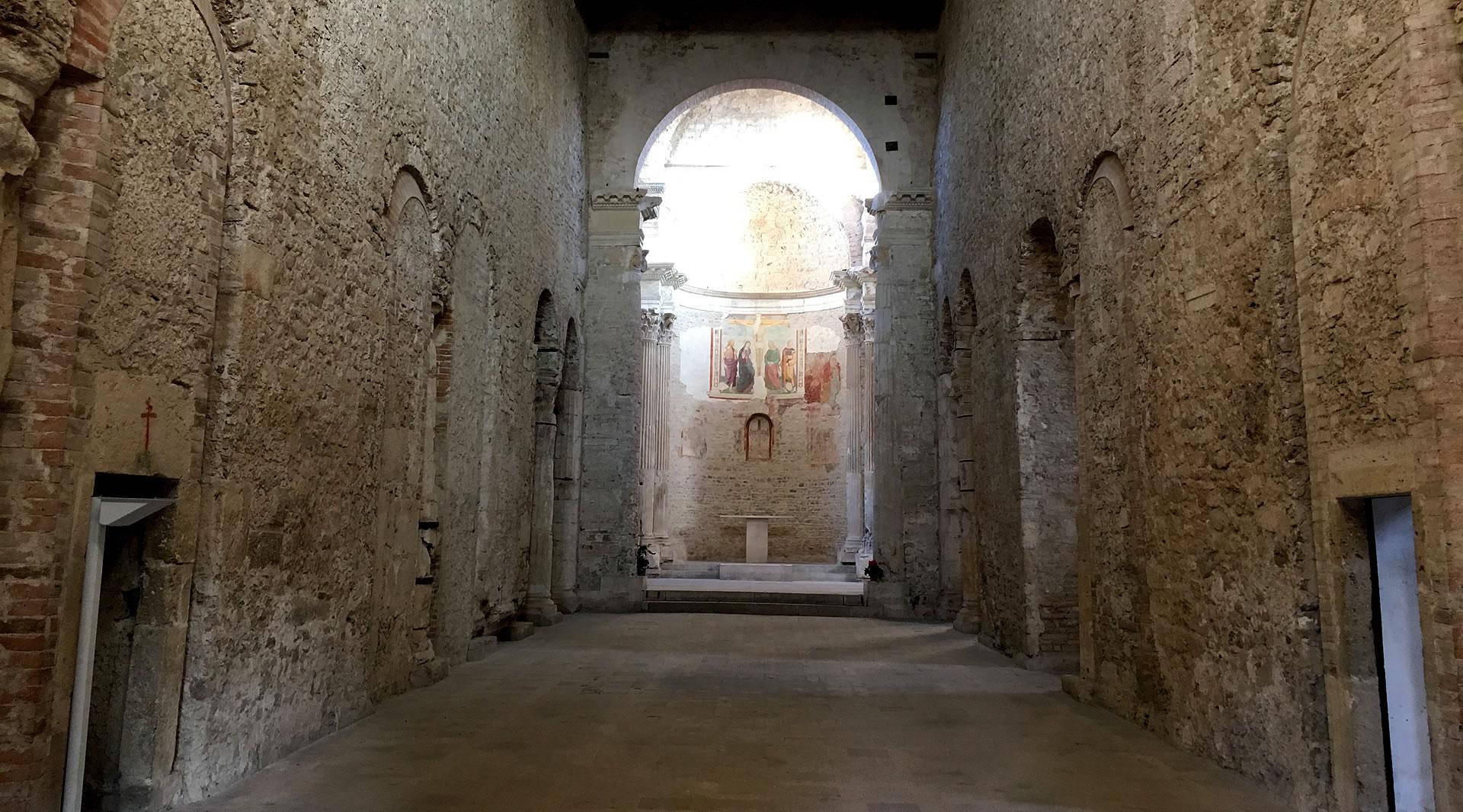 Stone central nave of the Basilica of San Salvatore, with frescoed apse and natural light illuminating the altar.