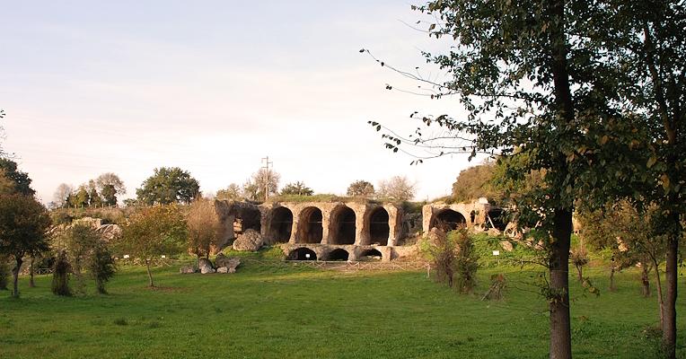 Resti monumentali delle grandi sostruzioni di Ocriculum, con arcate scavate nella roccia e vegetazione circostante
