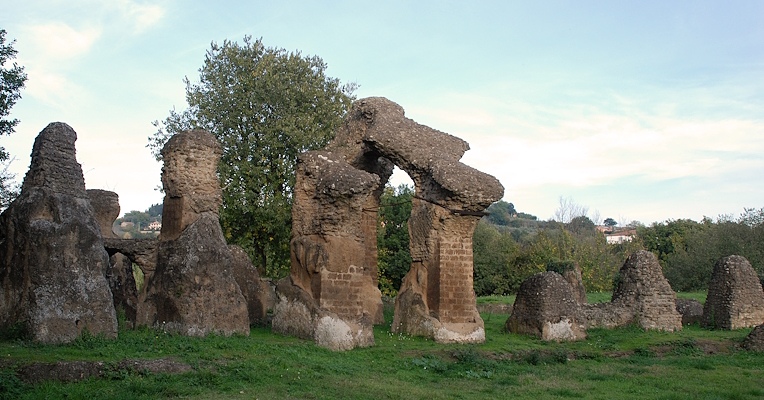 Ruines de l’amphithéâtre romain d’Ocriculum, avec des arcades en maçonnerie entourées d’herbe et d’arbres à l’arrière-plan