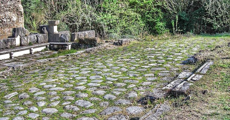 Roman paving with monuments and side channels, surrounded by vegetation