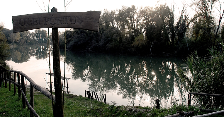 Vue sur le Tibre près d’Ocriculum, avec un panneau en bois indiquant le Port de l’Huile et des arbres reflétés dans l’eau