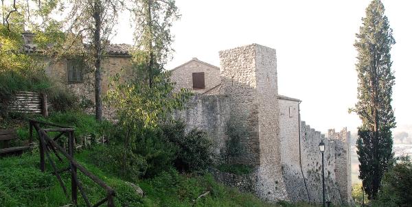  Side view of the Castle of Poggio di Otricoli with stone walls, a square tower, and vegetation along the slope. 