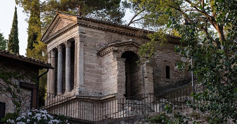 View of the Temple of Clitunno surrounded by greenery, with a front of four columns and a side entrance