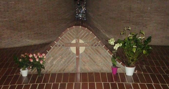 Tomb with a brick cross and the inscription "Mother Speranza of Jesus," decorated with flowers in white and colorful vases.