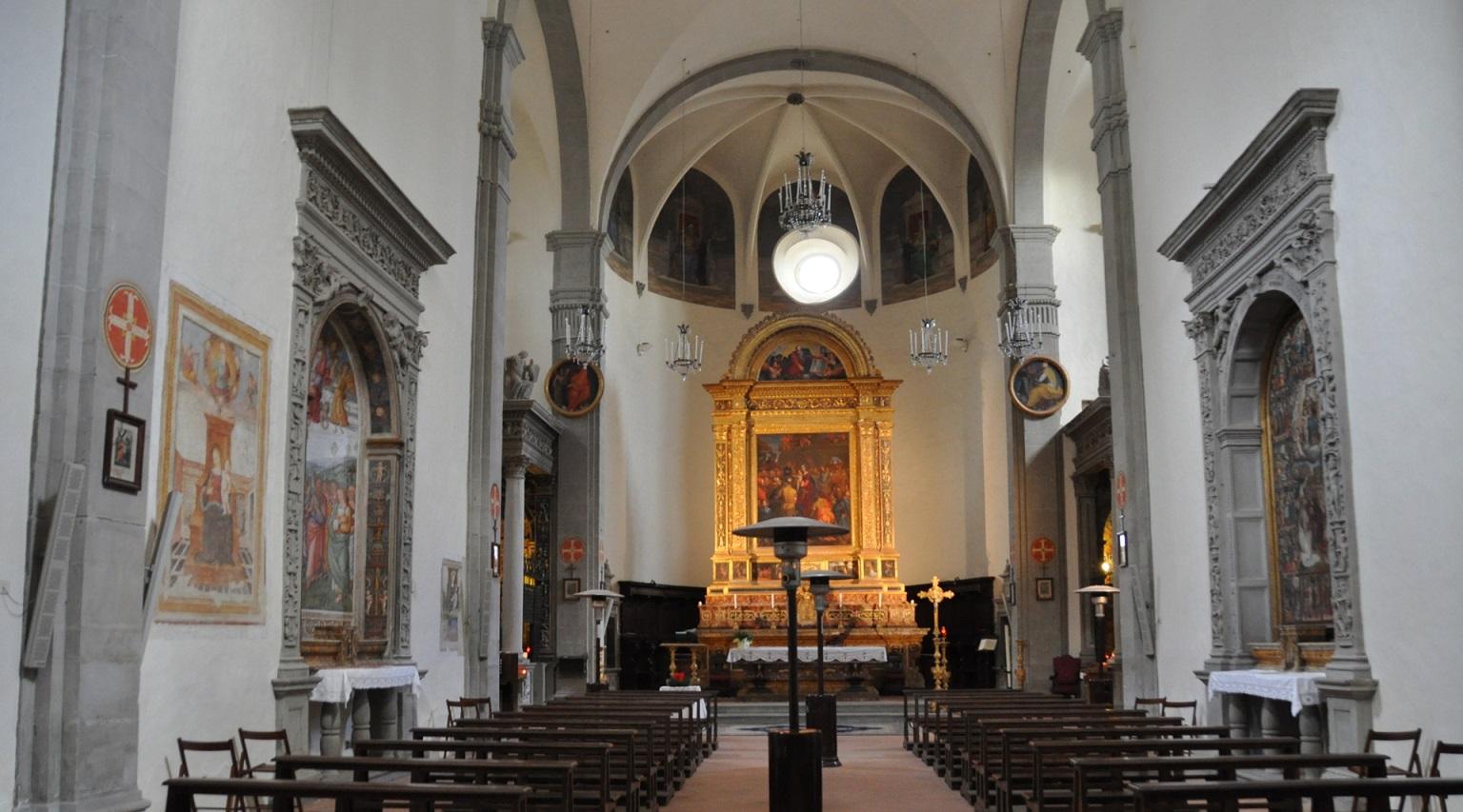 A view of the interior of the Sanctuary of Madonna dei Miracoli, where rows of benches for worshippers can be seen. The side walls are adorned with various paintings. In the background, there is the altar, topped by a significant painting framed in gold.