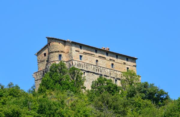  Rocca di Aries in Montone, majestätische mittelalterliche Festung, die aus der Vegetation unter klarem Himmel ragt. 