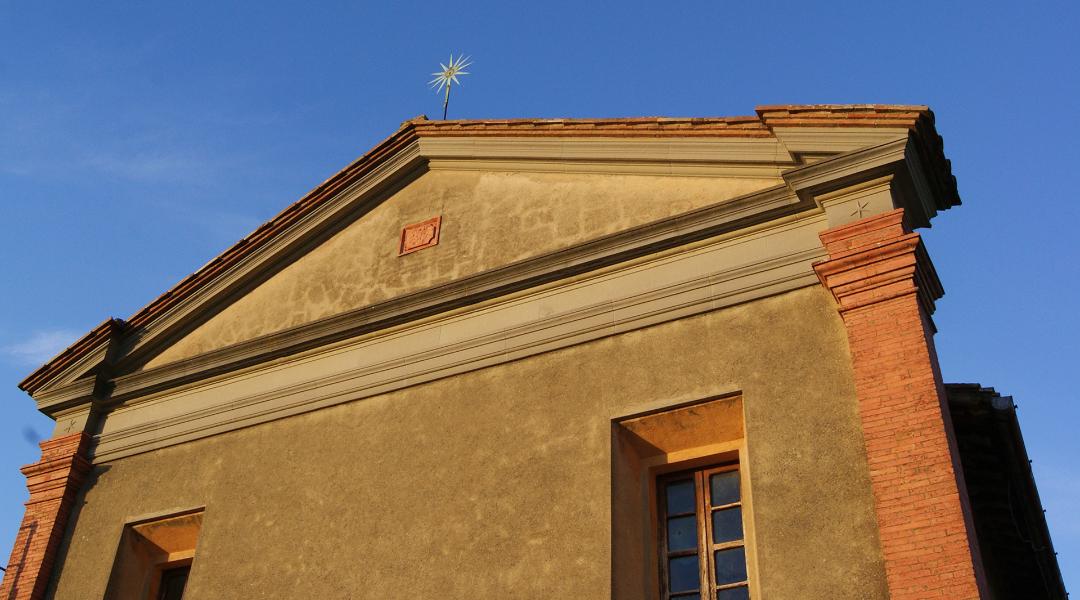 Façade of a yellow-plastered church with a gable roof, red brick corners, and a golden star on top.
