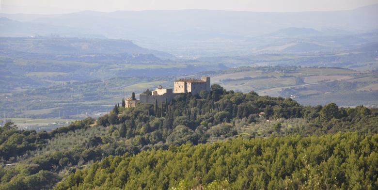  Panoramic view of Castello del Poggio nestled in the greenery of the Umbrian hills, with rolling countryside in the background. 