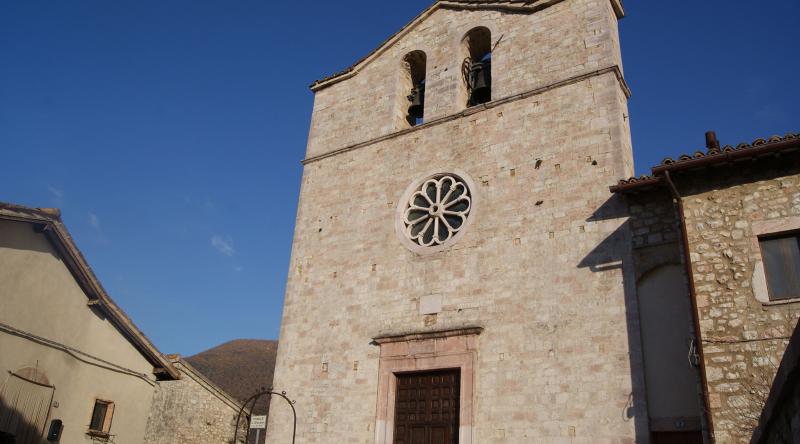 Facciata in pietra della chiesa di San Giovanni Battista a Vallo di Nera, con campanile a vela, rosone centrale e cielo sereno