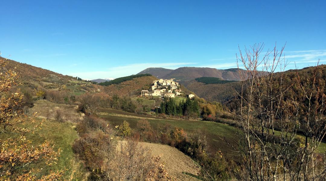 View of Usigni’s castle perched on a hill surrounded by green mountains, with autumn foliage and a clear sky.