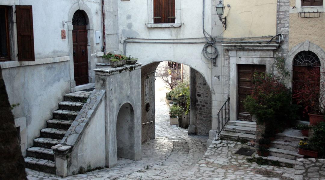 A stone alley with arches, stairways, and historic houses facing a stone-paved square.