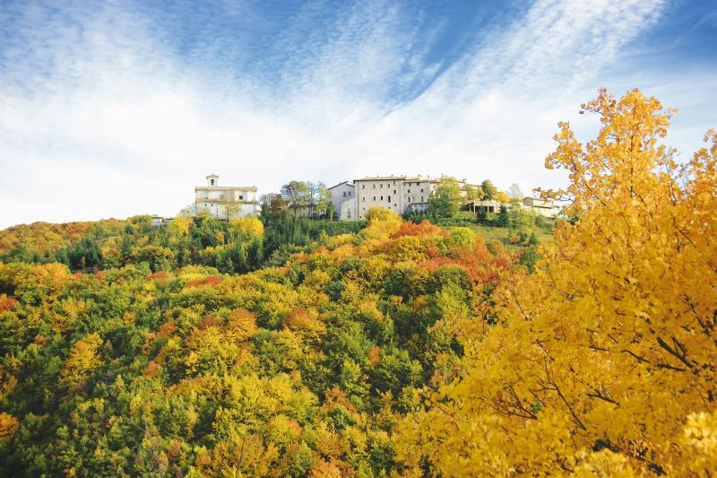 Vista di Usigni immerso nella vegetazione dai colori autunnali. Alla sinistra si scorge la chiesa di s. Salvatore.