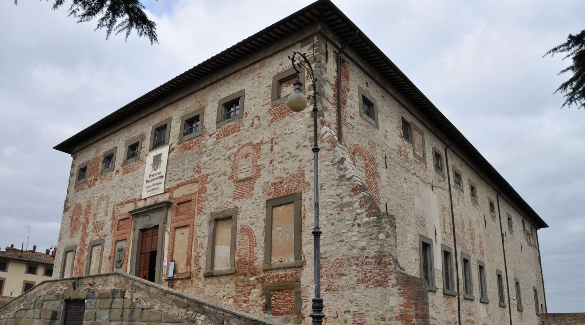 Vue d'angle du Palazzo della Corgna à Castiglione del Lago, avec la brique apparente, l'escalier extérieur et le lampadaire historique au premier plan.