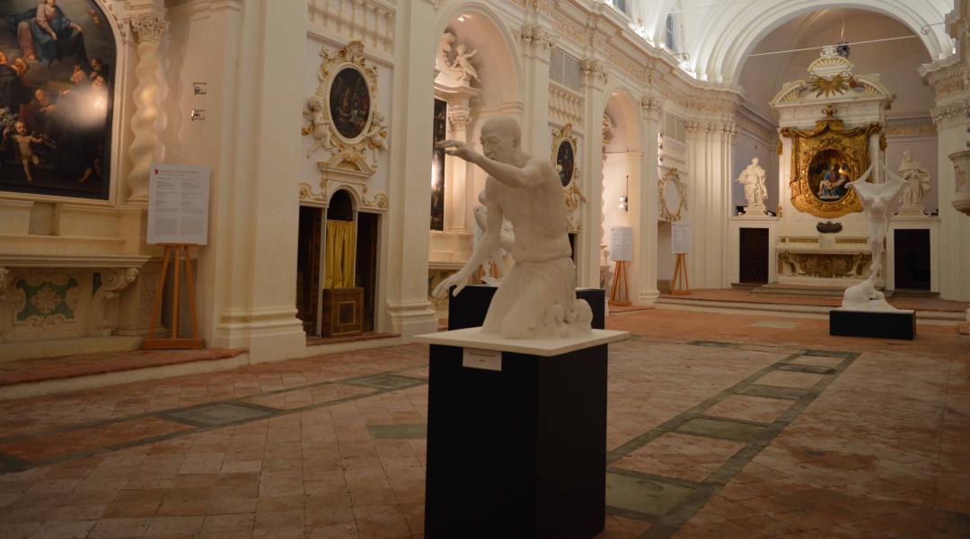 Veduta interna della chiesa di Santa Maria dei Servi, caratterizzata da decorazioni in stucco in stile barocco, un coro ligneo e un grande armadio della sacrestia. All'interno della chiesa, si notano varie sculture disposte al centro della sala. Sullo sfondo, l'altare barocco è affiancato da due statue in stucco, realizzate in stile berniniano.