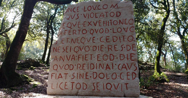 Steinkopie und rote Schrift der Lex Luci Spoletina im Inneren des Bosco Sacro