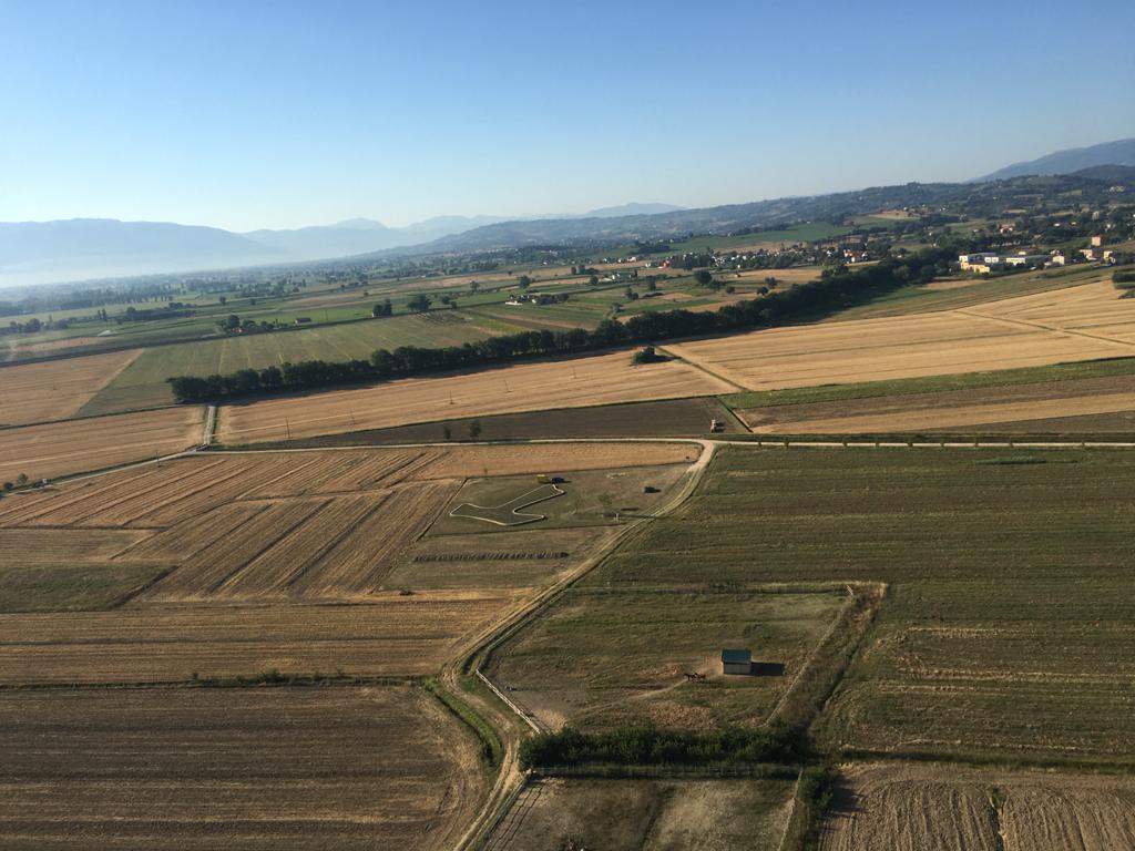Veduta aerea dei campi di Piandarca con il grande TAU francescano visibile al centro del paesaggio rurale.