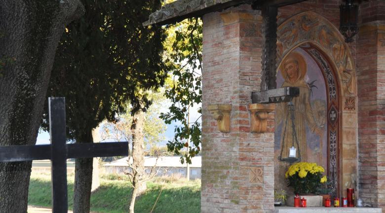 Immagine: Votive aedicule with a painting of Saint Francis, yellow flowers and red candles, among trees and greenery. 