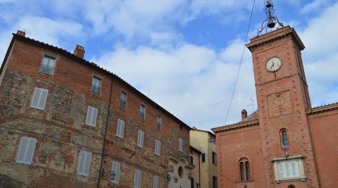 Monteleone di Orvieto’s Clock Tower in red brick with a sculpted façade, next to historic buildings.