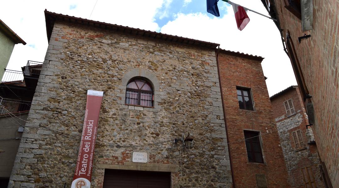 Stone façade of the Teatro dei Rustici in Monteleone di Orvieto, with an arched window, on a village street.