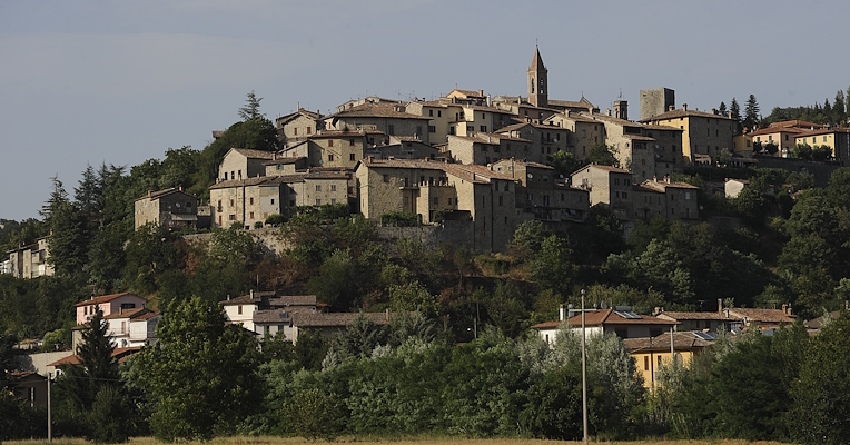 Medieval village of Pietralunga perched on a hill, with stone houses, a bell tower, and lush vegetation in the background.