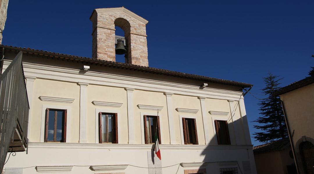 Facade of Sellano’s town hall, a historic building with framed windows and a stone bell tower above the roof, under a clear sky.