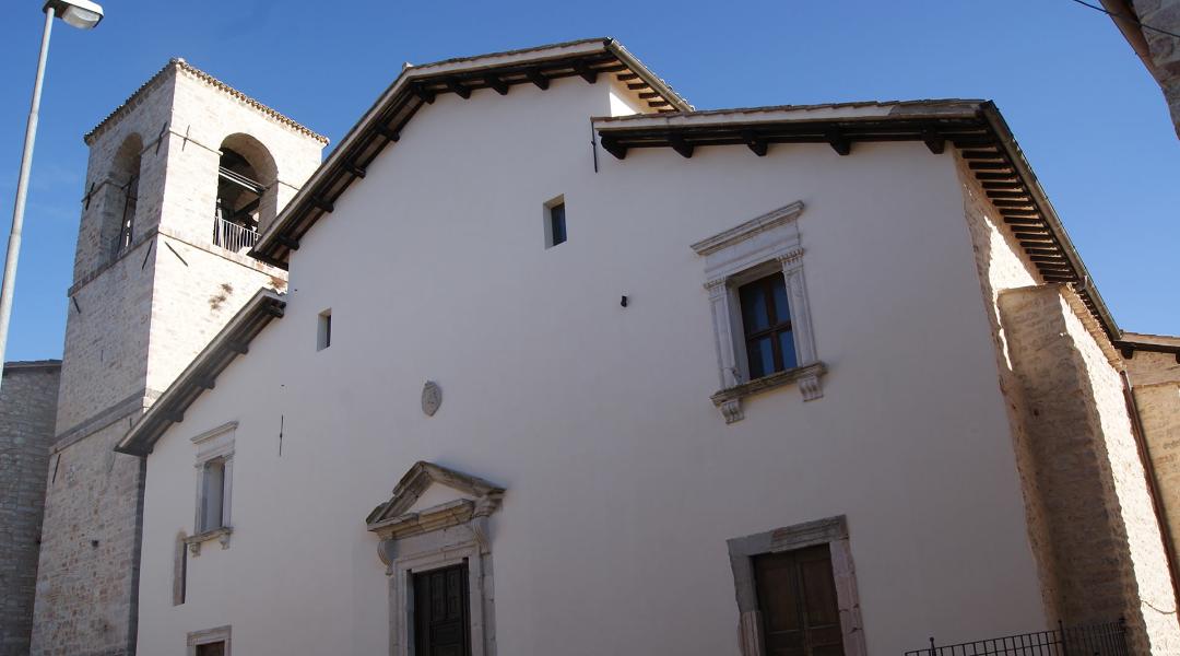 Facade of the Church of San Francesco in Sellano, with a stone bell tower and architectural details, under a clear sky.