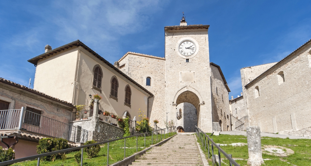 Stairway leading to the Clock Tower of Monteleone di Spoleto, surrounded by stone buildings and a clear Apennine sky.