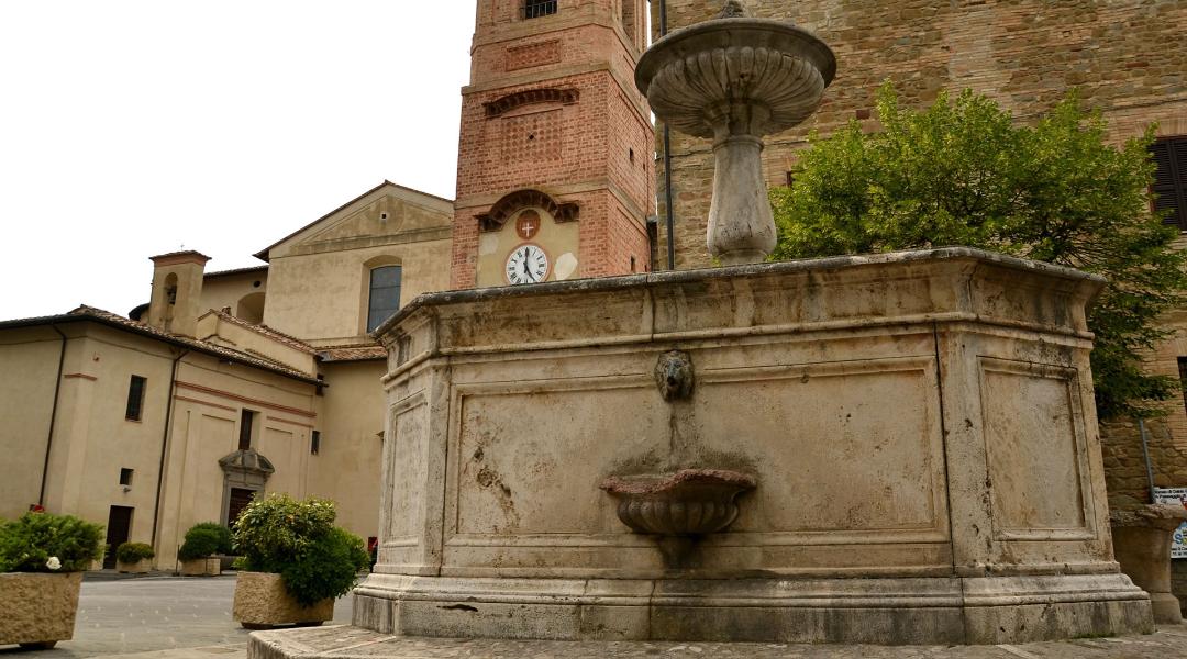 Stone fountain in Piazza Cavour, Bettona; in the background, the clock tower and the church of Santa Maria Maggiore.