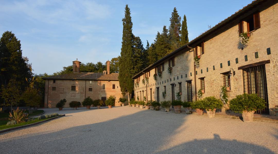Rural stone complex surrounded by greenery in Deruta, with courtyard and flower pots along the façade.