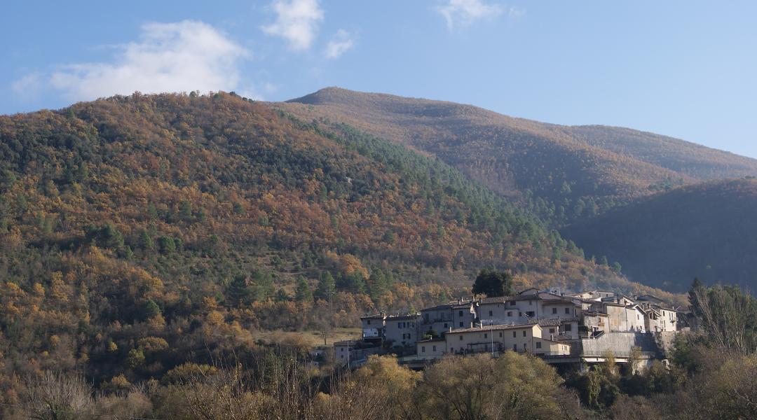 Medieval village perched among the Umbrian hills, immersed in the autumn colours of the Valnerina under a clear sky.