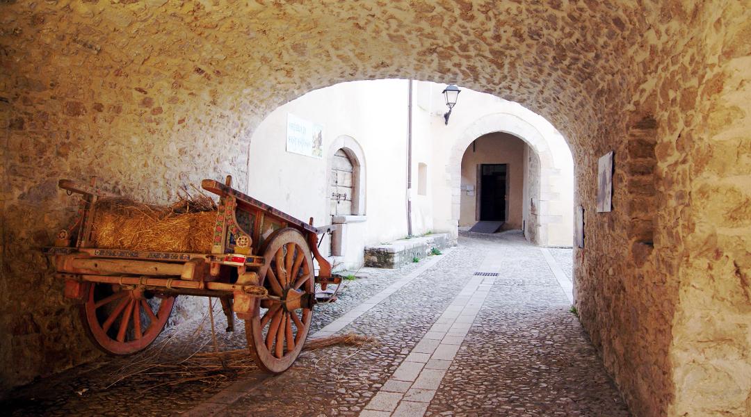 Ancient stone passage in Sant'Anatolia di Narco with a rustic cart and a cobbled street leading to a courtyard.