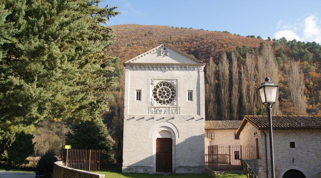 Romanesque facade of the Abbey of Saints Felice and Mauro, nestled in the greenery of the Valnerina at the foot of the hills.
