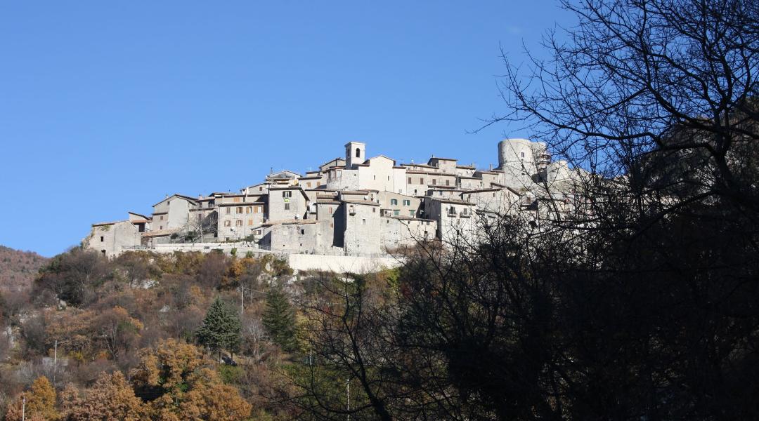 Panoramic view of Polino, a medieval village perched on a hill, with stone houses and a circular tower.