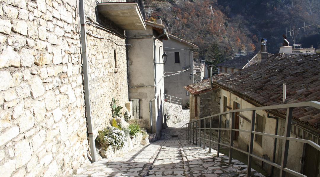 Stone-paved alley in the village of Polino, lined with old houses featuring terracotta roofs and iron railings.
