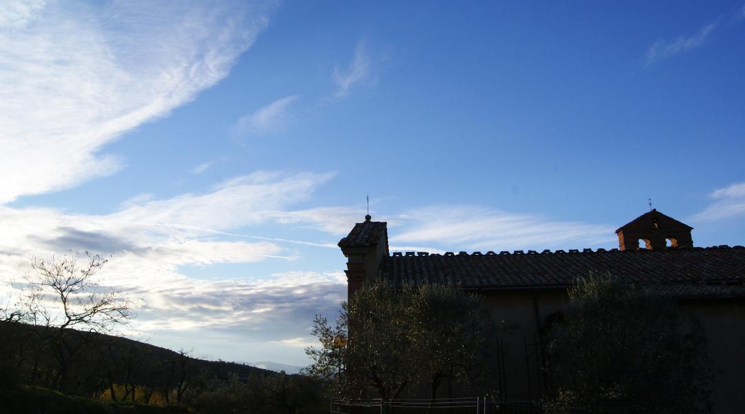 Silhouette of a church with a bell gable at sunset, surrounded by trees and hills, under a sky with thin clouds.