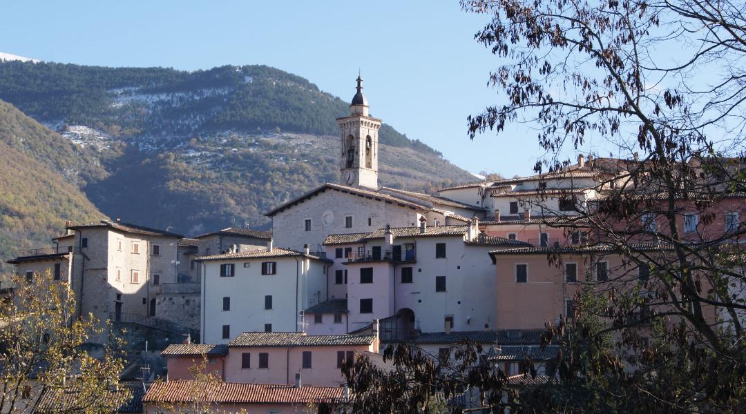 Stone houses and the bell tower of Preci stand out among snow-capped, wooded mountains in a peaceful Umbrian winter landscape.