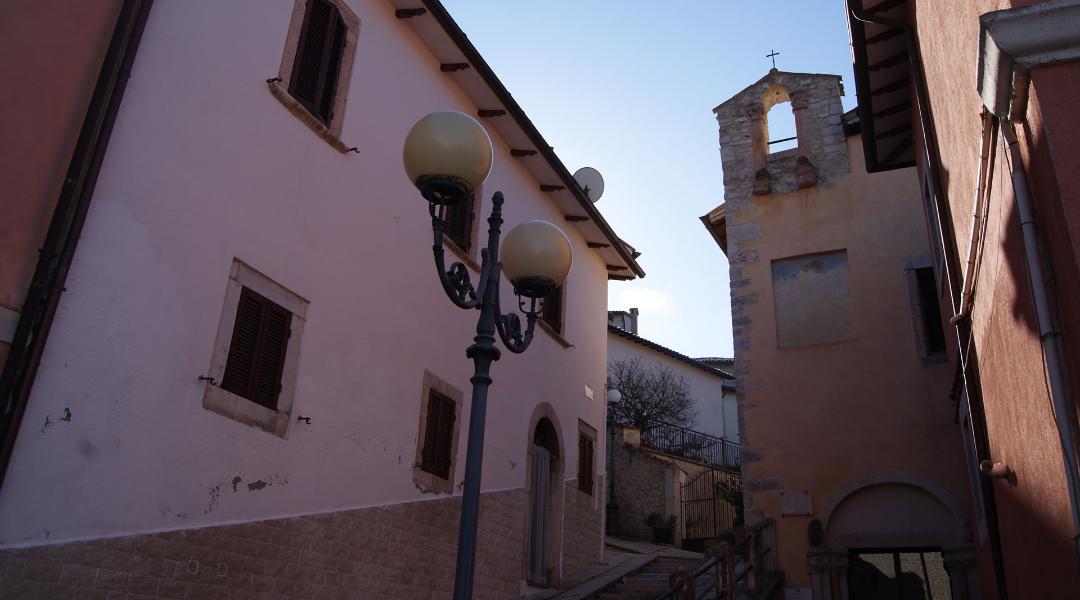 Glimpse of Preci’s historic center, with quiet alleys, stone buildings and a small church with a gabled bell tower.