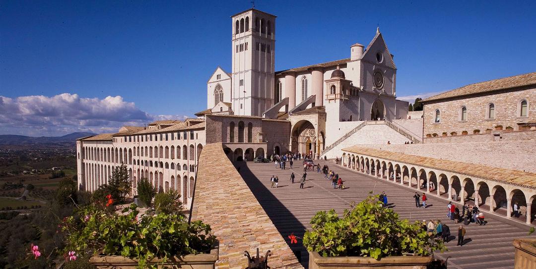 Basilica of Saint Francis in Assisi with its imposing staircase and arches, with visitors on a sunny day