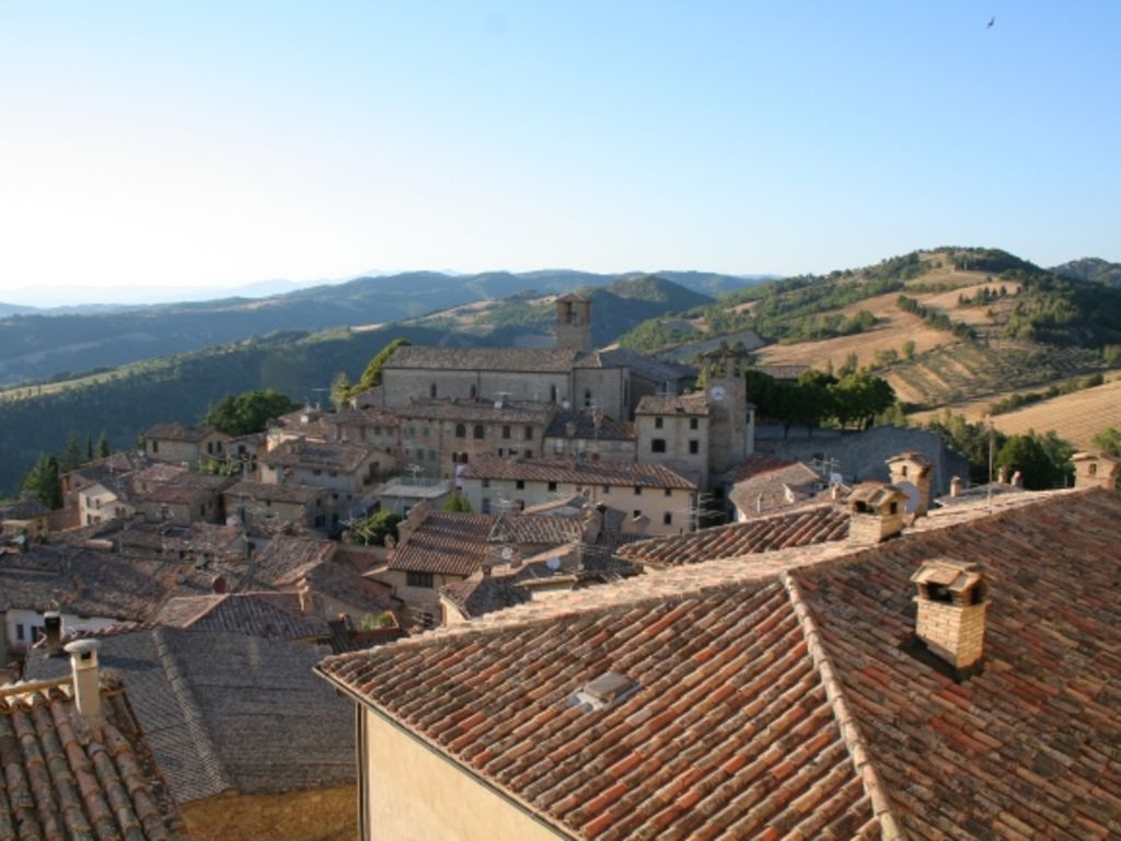 Panoramic view of Montone with terracotta roofs of the medieval village, surrounded by green hills.