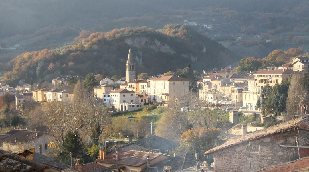 Panorama of Ferentillo, nestled among green hills, with a bell tower rising above the houses bathed in golden light.